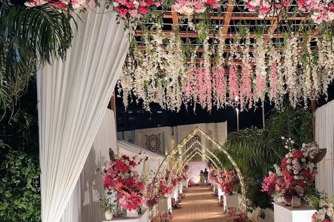The pergola walkway at night, dressed with fuchsia and white flowers and lit arches.