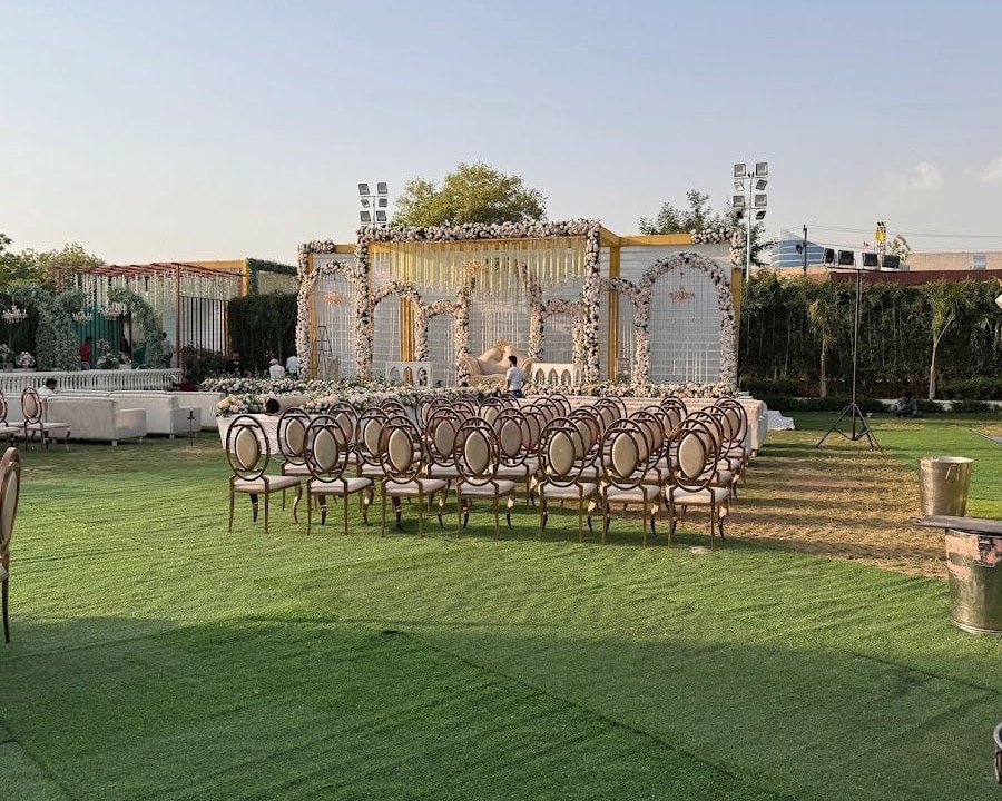 The lawn set for a ceremony in late afternoon light: a white and gold floral pavilion and rows of cream-cushioned gold chairs.