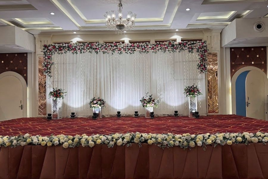 The hall stage dressed for a reception: a white sheer backdrop under a floral arch and a chandelier.