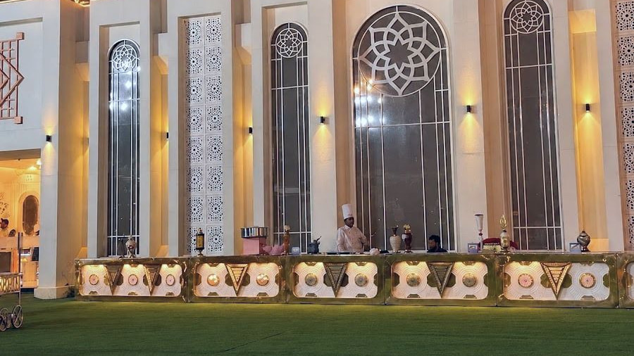 The cream façade at night with tall arched windows and gold live counters on the lawn.